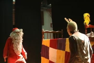 scena con attore travestito da Babbo Natale e un grande letto e un altro attore travestito da personaggio di fantasia con cappellino da renna