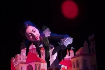 scena con attrice e un castello cartonato con figure cartonate dell'epoca e un pipistrello sul fondo una luna